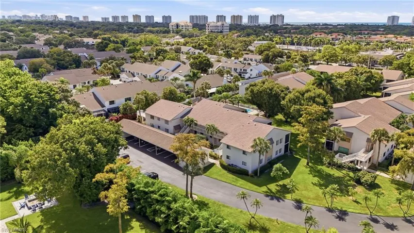 Aerial perspective of multi-family structures featuring shingled roofs, covered parking carports, exterior balconies, and established landscaping with mature trees
