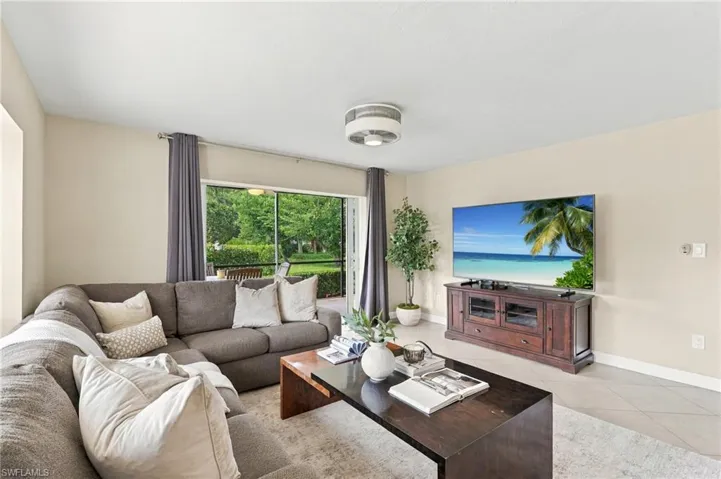 Living room featuring large-format tile flooring, a central ceiling-mounted light fixture, and sliding glass doors opening to a screened outdoor area