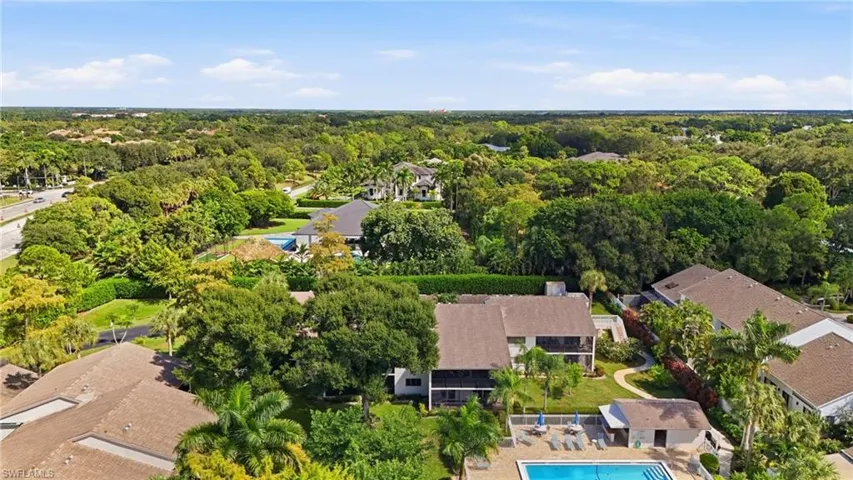 Aerial perspective of a multi-structure property featuring mature trees, landscaped grounds, and a central swimming pool