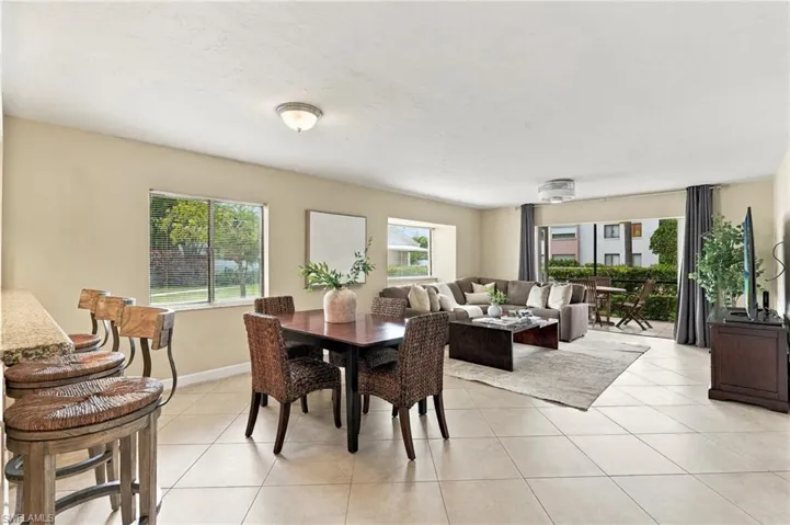 Open-concept living space featuring large-format tile flooring, a built-in breakfast bar with stone-surfaced countertop, recessed lighting, and expansive glass sliding doors