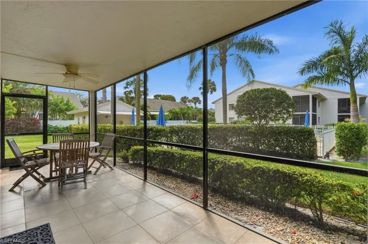 Screened-in lanai featuring neutral tile flooring, a ceiling fan, and direct exposure to a landscaped lawn with mature palm trees
