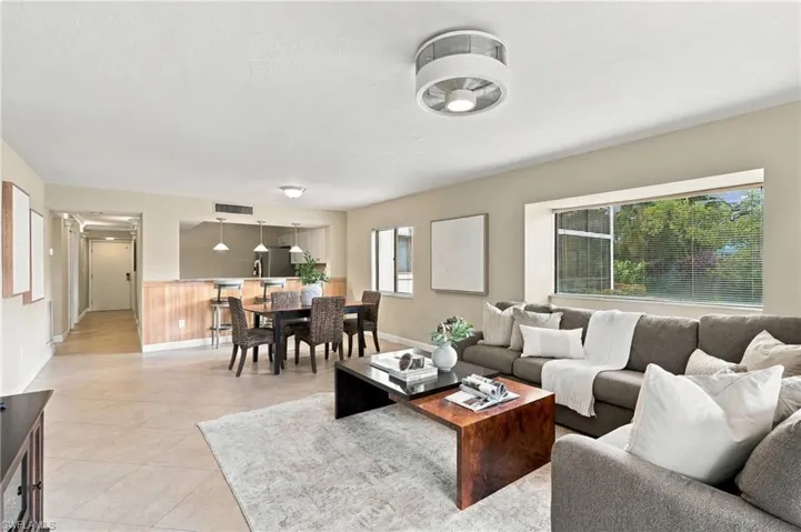Open-concept interior featuring large-format tile flooring, recessed lighting, a modern ceiling fan, and a pass-through kitchen window with a breakfast bar