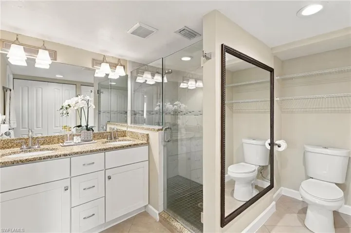 Dual-sink vanity with stone countertop, glass-enclosed shower, built-in wire shelving, and tile flooring