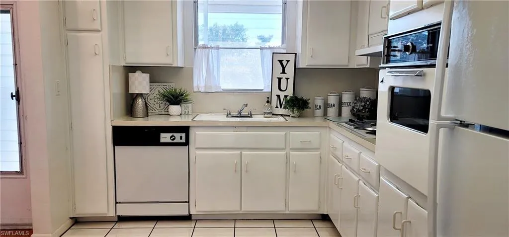 Kitchen featuring white cabinetry, white appliances, a healthy amount of sunlight, and light tile patterned flooring
