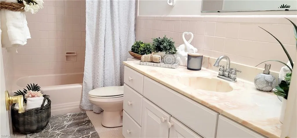 Full bathroom featuring tile walls, vanity, toilet, and shower / bathtub combination with curtain