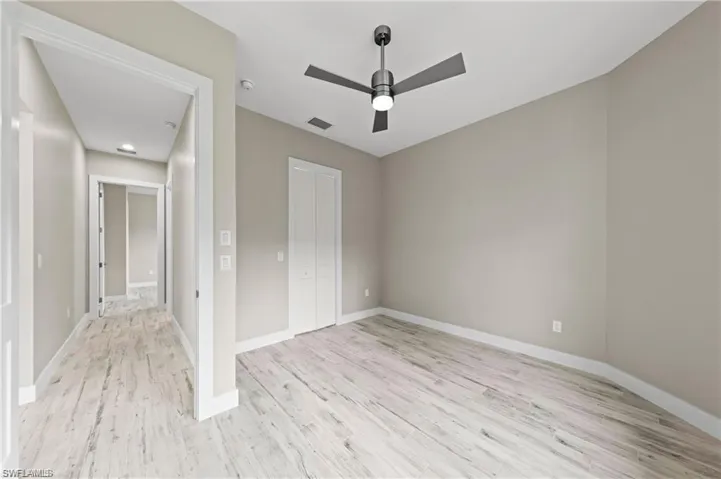 Guest bedroom with a walk-in closet with wood shelving, a ceiling fan, and light wood-style flooring