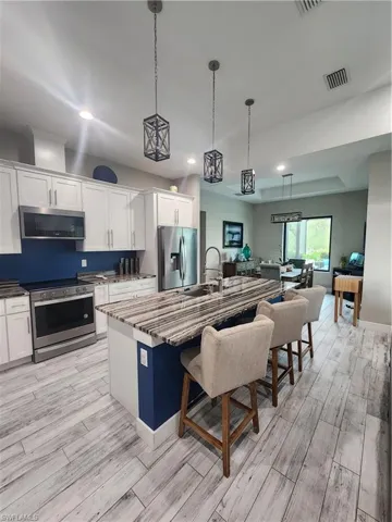 Kitchen with an 8ft 4in island, range, hanging light fixtures, white cabinetry, and stainless steel appliances