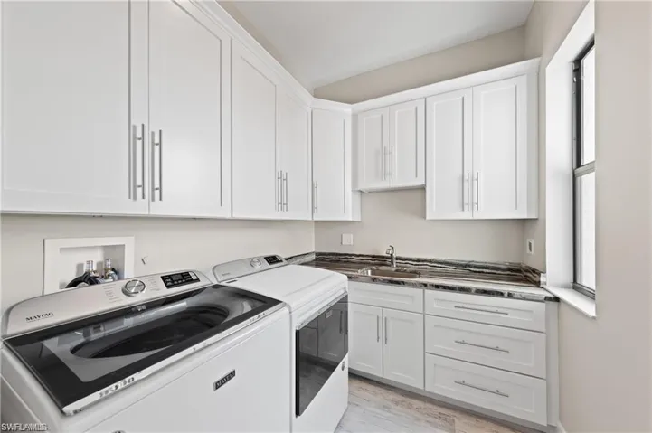 Laundry area with washer and dryer, cabinet space, and light wood-style flooring