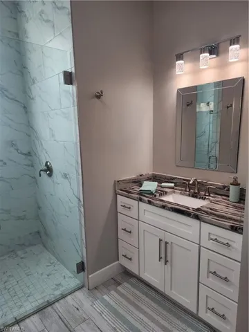 Full bathroom with a marble finish shower, vanity, and wood finish floors