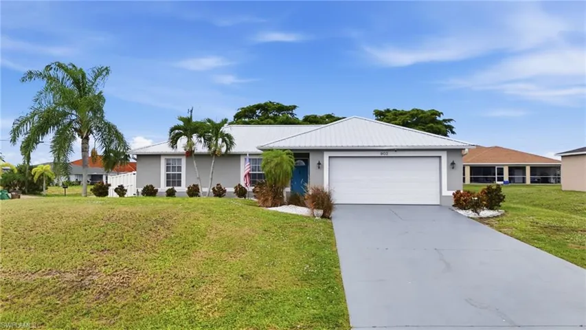 Ranch-style house featuring driveway, a front yard, an attached garage, stucco siding, and a metal roof