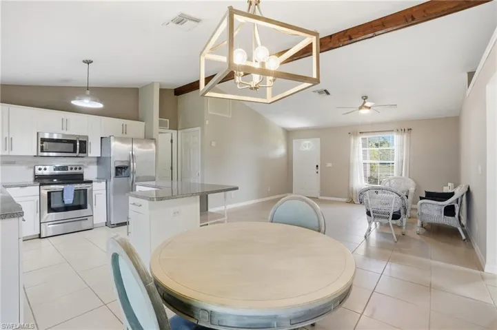 Dining area featuring beamed ceiling, a chandelier, high vaulted ceiling, light tile patterned floors, and a ceiling fan