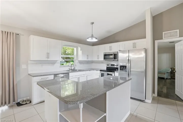 Kitchen featuring stainless steel appliances, vaulted ceiling, tasteful backsplash, white cabinetry, and open shelves