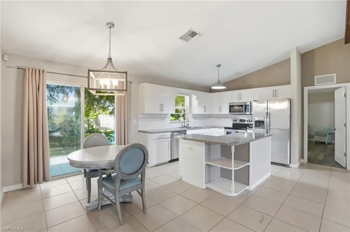 Kitchen with appliances with stainless steel finishes, pendant lighting, a kitchen island, dark stone counters, and lofted ceiling