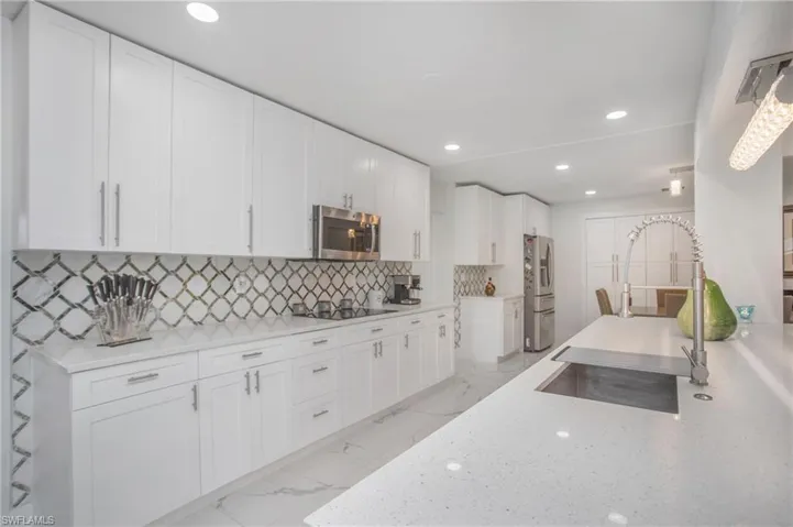 White shaker cabinetry, patterned tile backsplash, stainless steel appliances, solid surface countertops, and recessed lighting