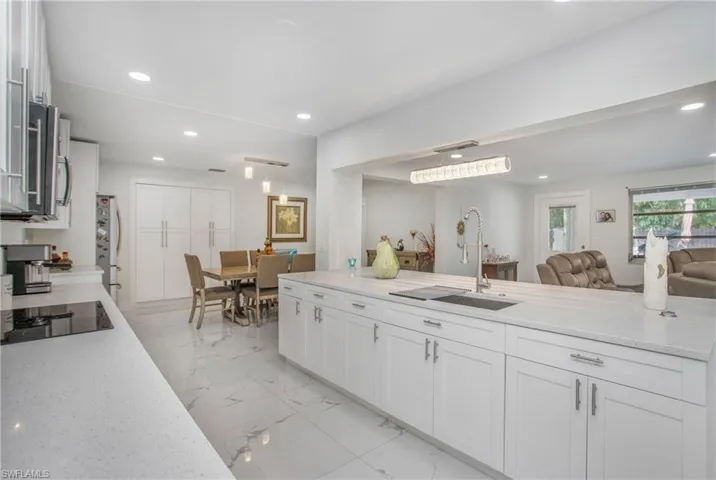 Kitchen featuring white cabinetry, light-toned countertops, a built-in cooktop, and a stainless steel sink with a gooseneck faucet