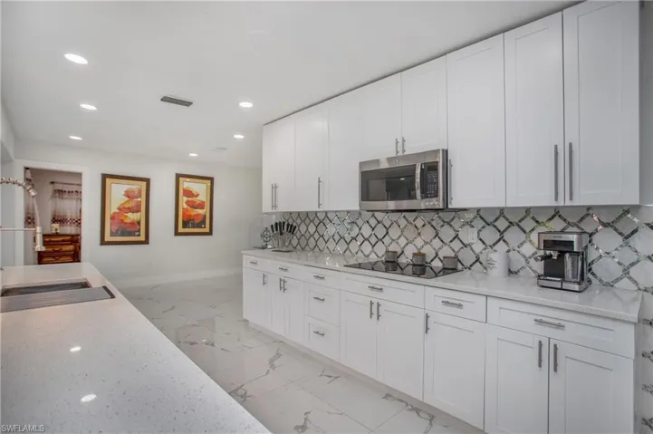White shaker-style cabinetry with stainless steel hardware, integrated stainless steel microwave, cooktop, and a patterned tile backsplash