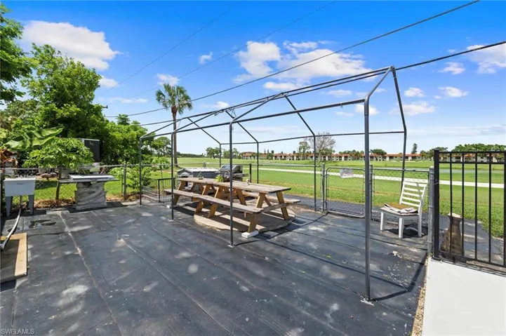 Outdoor patio space featuring a metal frame structure, black ground covering, and chain-link fencing