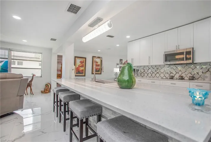 White cabinetry with stainless steel appliances, mosaic tile backsplash, and a large central island with seating