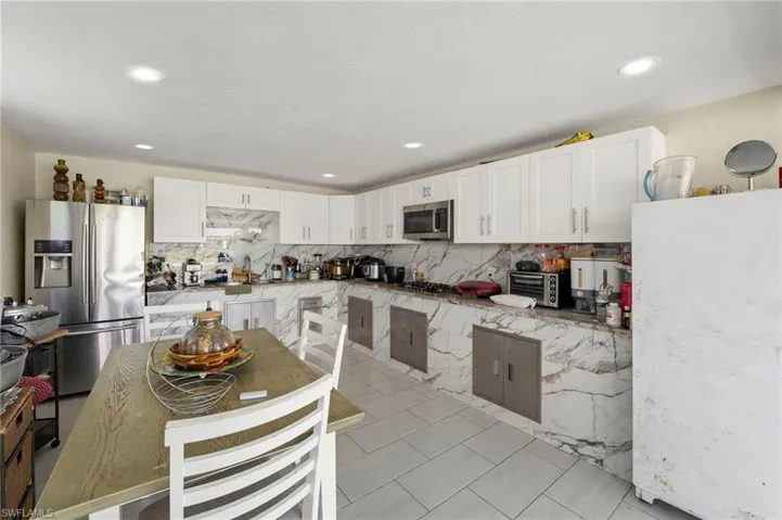 White shaker cabinetry, marble-patterned backsplash and countertops, recessed lighting, and tile flooring