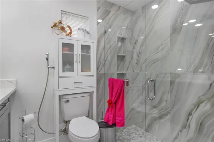 Glass-enclosed shower with marbled tile surround, built-in shower niche, and pebbled floor