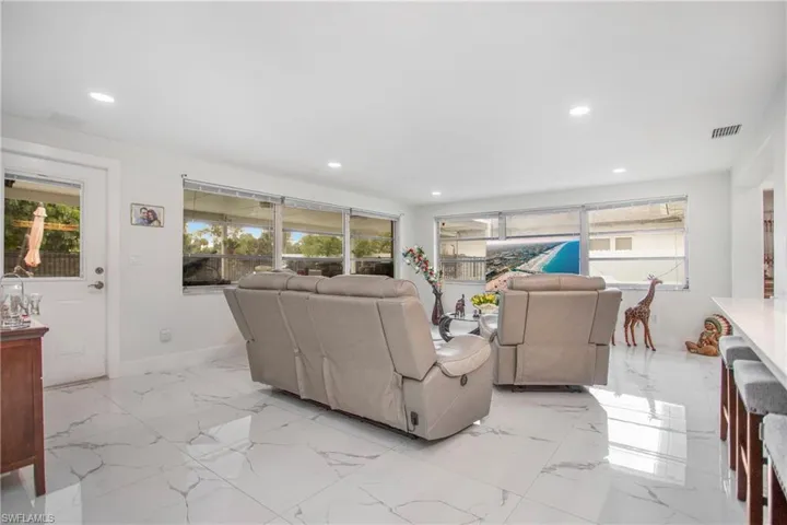 White tile flooring with grey veining, recessed lighting, white walls, multiple windows, and a white interior door with a glass panel