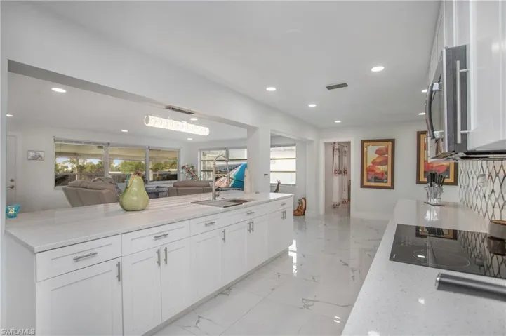 Modern kitchen featuring white cabinetry, light-toned countertops, a built-in cooktop, and a stainless steel microwave