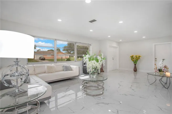 Spacious living area featuring polished tile flooring, recessed lighting, and a large window providing abundant natural light