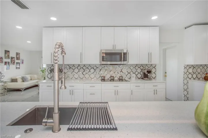 Modern kitchen featuring white cabinetry, a patterned tile backsplash, stainless steel appliances, a large sink with a coil spring faucet, and recessed lighting