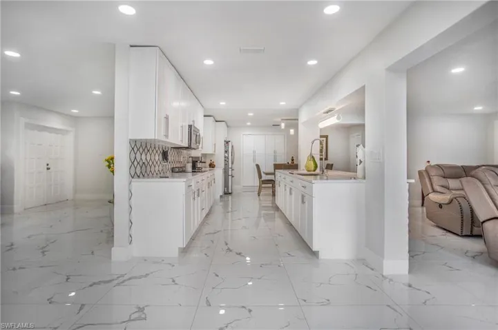 Modern kitchen featuring white cabinetry, stainless steel appliances, a patterned backsplash, and marbled floor tile