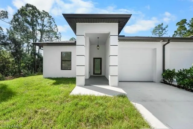 Contemporary house with a front yard, concrete driveway, stucco siding, and a garage