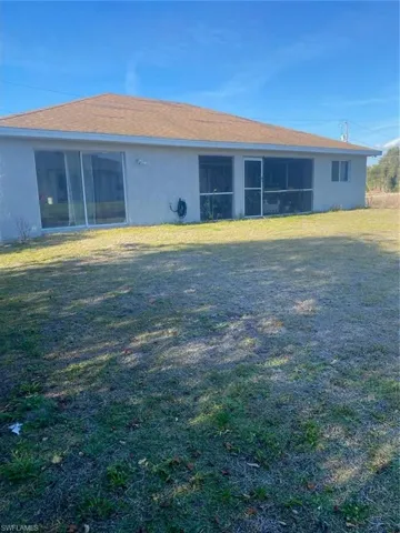 Back of house with a lawn, stucco siding, a shingled roof, and a sunroom