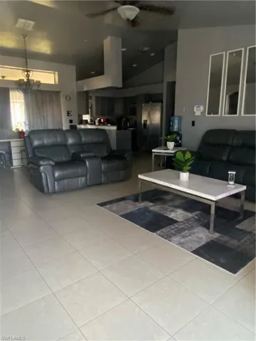 Living area featuring vaulted ceiling, light tile patterned flooring, and ceiling fan