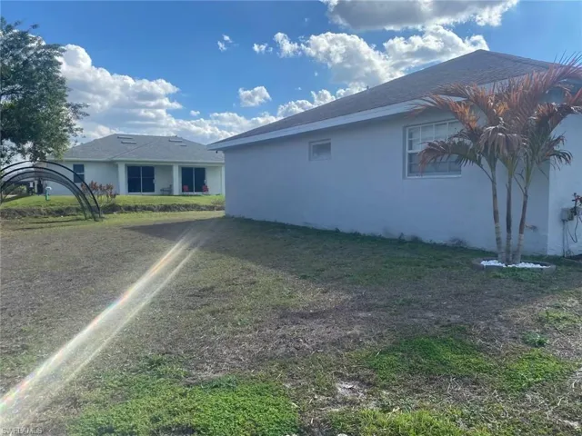 View of side of property featuring stucco siding, a yard, and roof with shingles