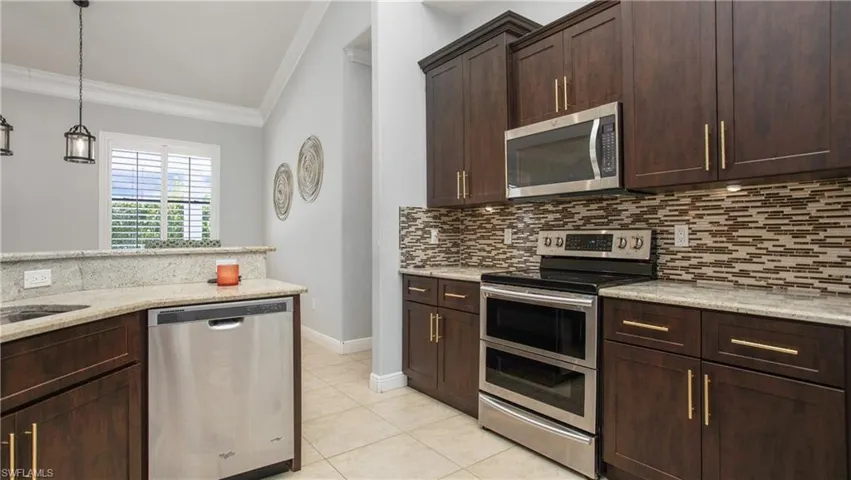 Kitchen featuring appliances with stainless steel finishes, ornamental molding, backsplash, light tile patterned floors, and dark brown cabinetry