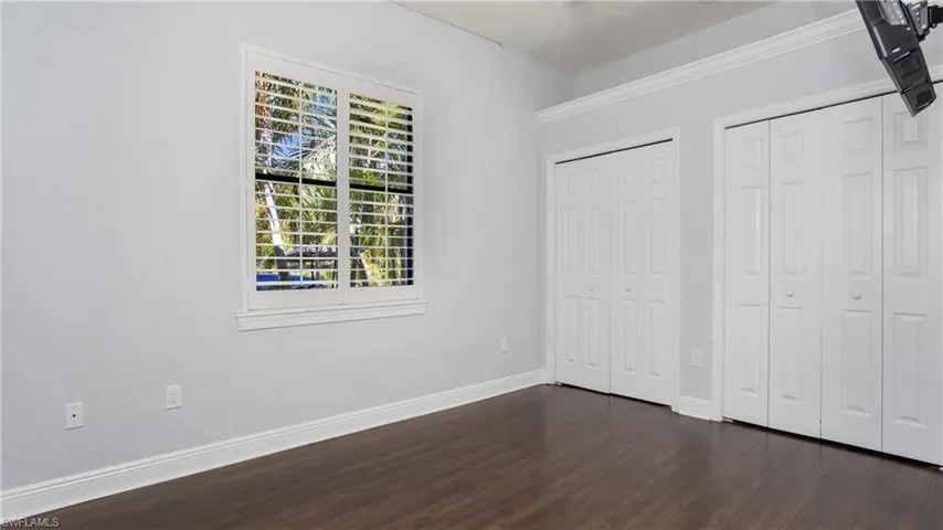 Unfurnished bedroom with dark wood-style floors, two closets, and baseboards