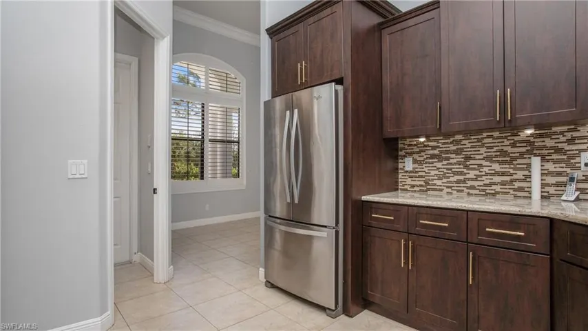 Kitchen with freestanding refrigerator, crown molding, decorative backsplash, baseboards, and light tile patterned floors