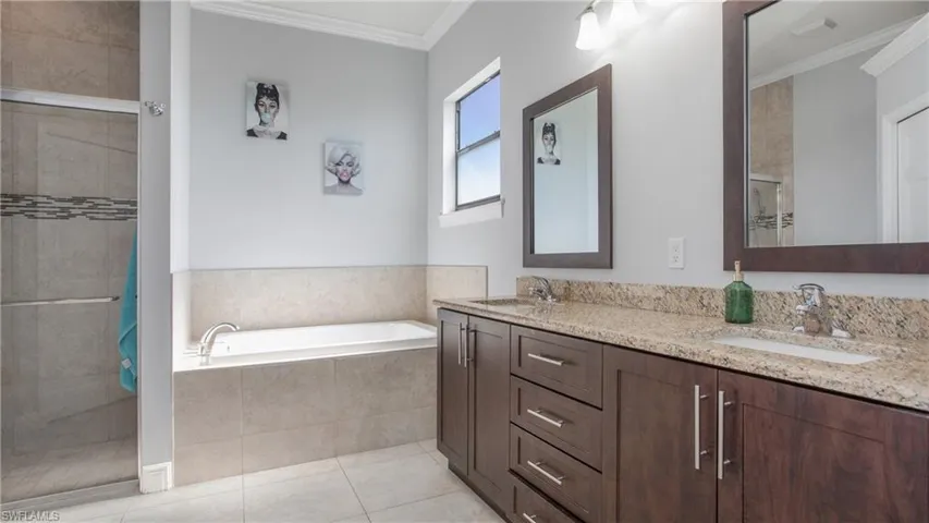 Bathroom with a tile shower, crown molding, a garden tub, double vanity, and tile patterned floors