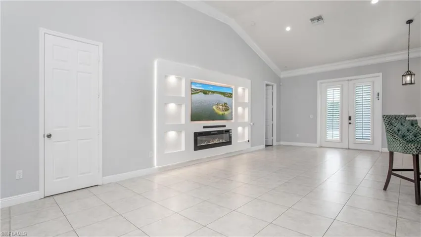 Unfurnished living room featuring french doors, a glass covered fireplace, light tile patterned flooring, ornamental molding, and baseboards