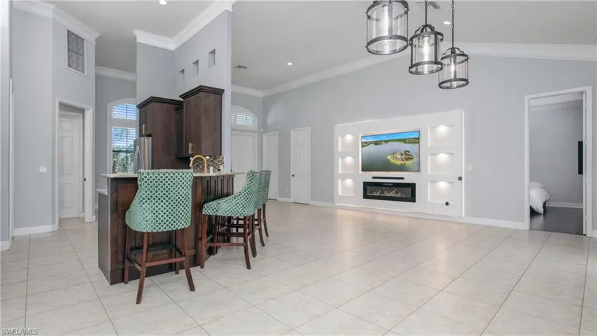 Dining room with a high ceiling, light tile patterned flooring, ornamental molding, baseboards, and a glass covered fireplace