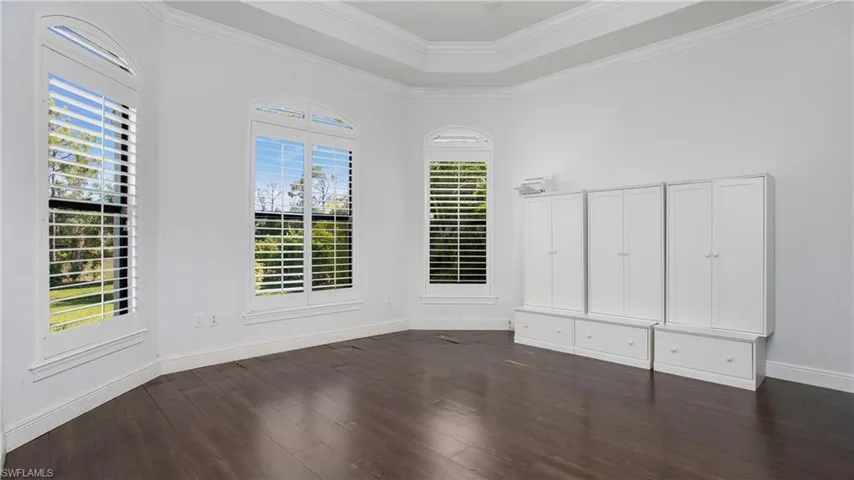 Empty room with dark wood-style floors, baseboards, ornamental molding, and a raised ceiling