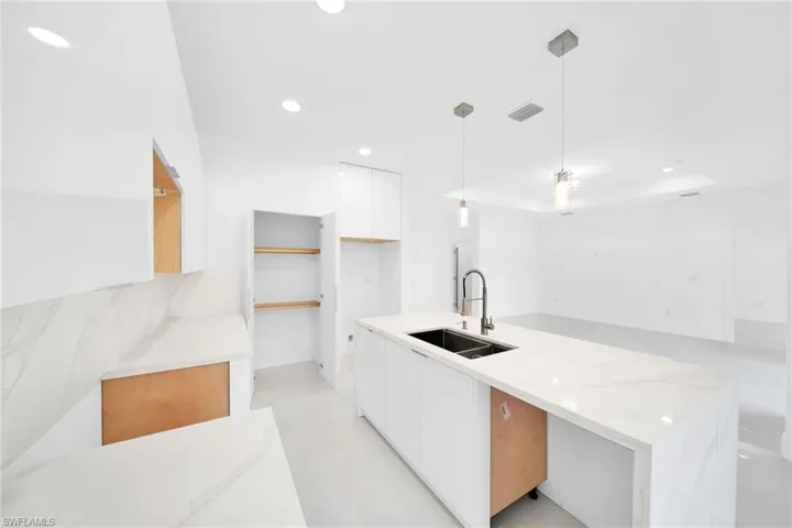 Kitchen with white cabinetry, light tile patterned flooring, hanging light fixtures, sink, and light stone counters