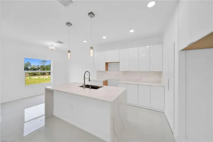 Kitchen featuring sink, hanging light fixtures, decorative backsplash, light stone countertops, and white cabinetry