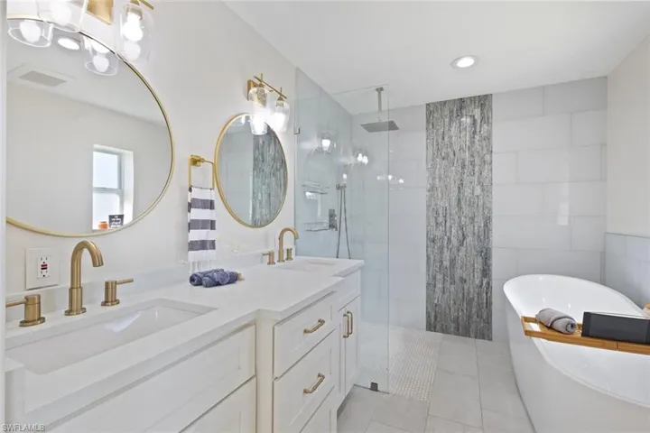Bathroom featuring walk in shower, double vanity, a freestanding tub, tile patterned flooring, and tile walls