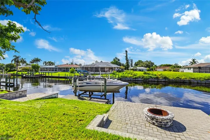 Dock area featuring boat lift, an outdoor fire pit, a water view, and a residential view