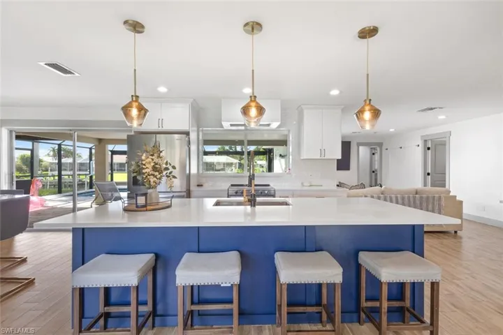 Kitchen with light wood finished floors, a center island with sink, white cabinetry, freestanding refrigerator, and recessed lighting