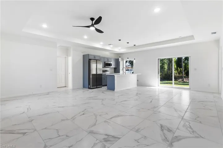 Unfurnished living room with ceiling fan, sink, and a tray ceiling