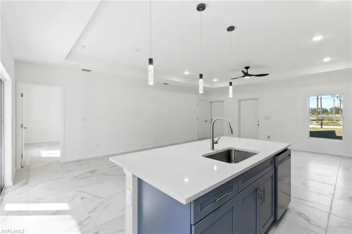 Kitchen featuring dishwasher, decorative light fixtures, sink, ceiling fan, and a tray ceiling