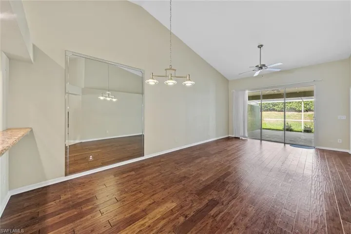 Spare room with hardwood / wood-style floors, ceiling fan with notable chandelier, and high vaulted ceiling