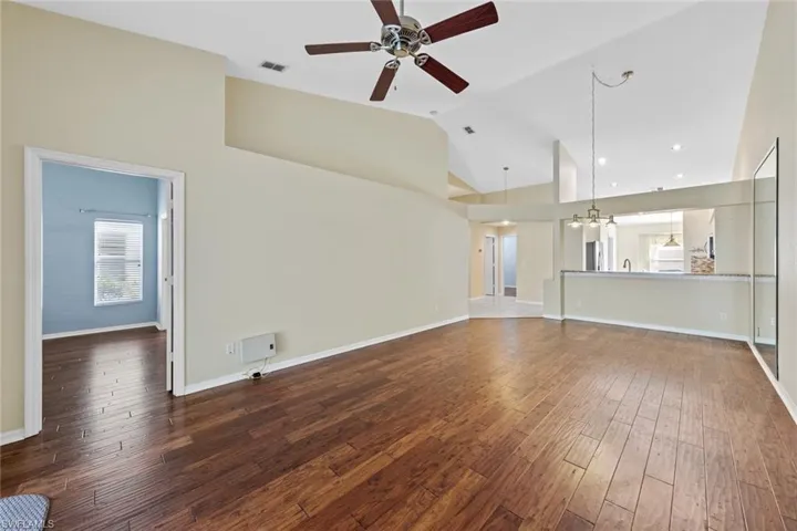 Unfurnished living room featuring high vaulted ceiling, dark wood-type flooring, and ceiling fan