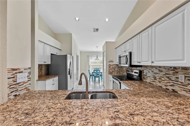 Kitchen featuring stainless steel appliances, backsplash, decorative light fixtures, sink, and white cabinets